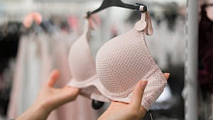 Someone bra shopping and holding a light pink padded underwire bra.