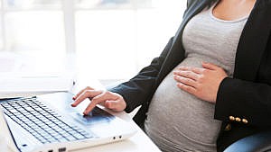 A pregnant lady working on her computer laptop while lightly placing her hands on her belly.