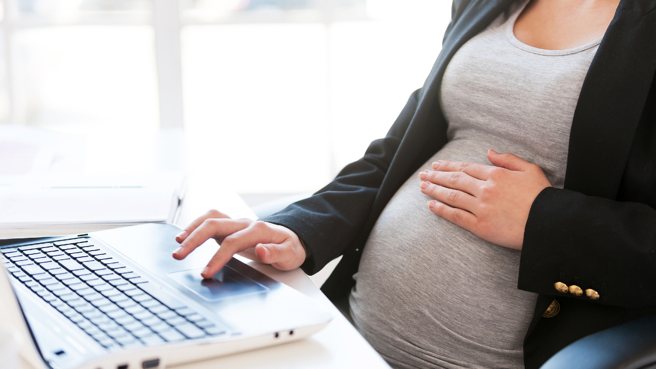 A pregnant lady working on her computer laptop while lightly placing her hands on her belly.
