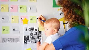 mom holding baby while writing on a wall calendar