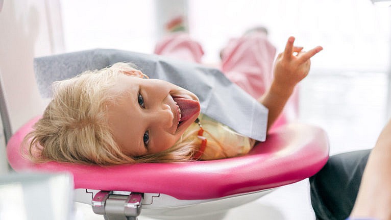 Picture of a girl sticking her tongue out and showing a peace sign at dentist office.