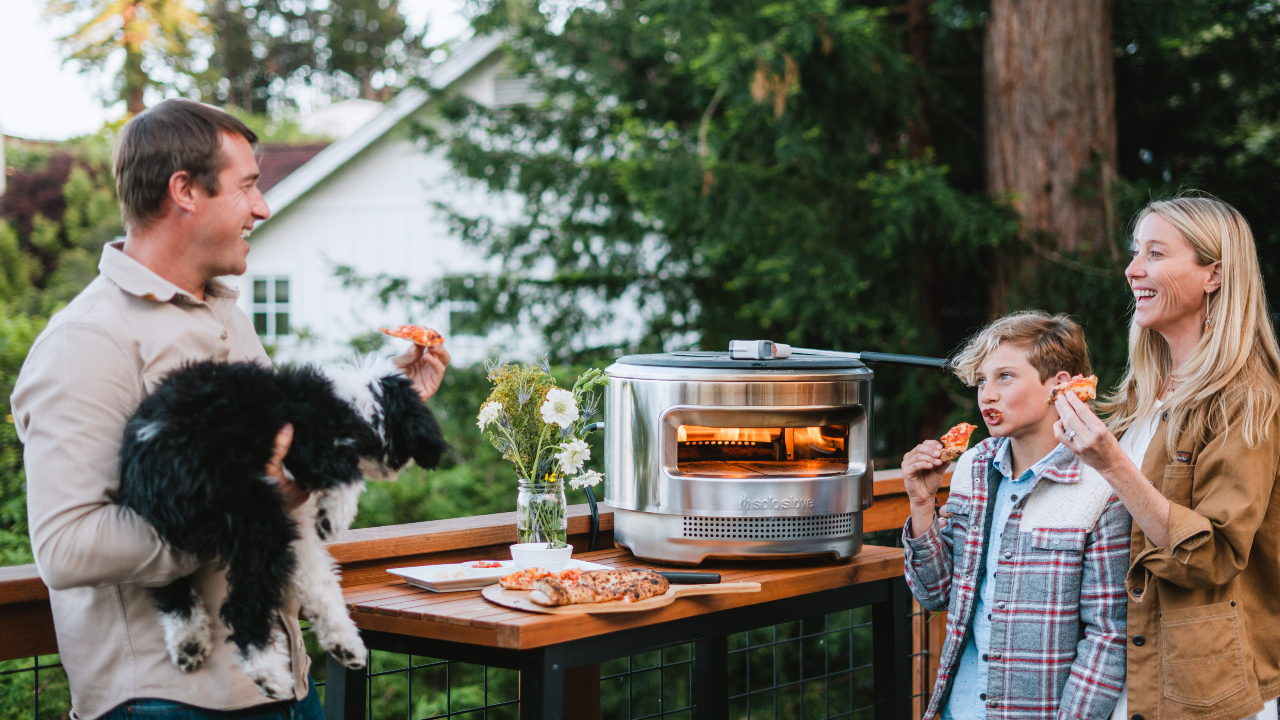 lifestyle image of a family enjoying a pizza outdoors next to a stainless steel outdoor pizza oven