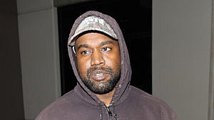 A picture of Kanye West in a grey hoodie and wearing a cap.