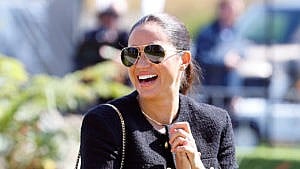 Meghan Markle wearing sunglasses and a sleek ponytail while holding her hands to her chest while smiling