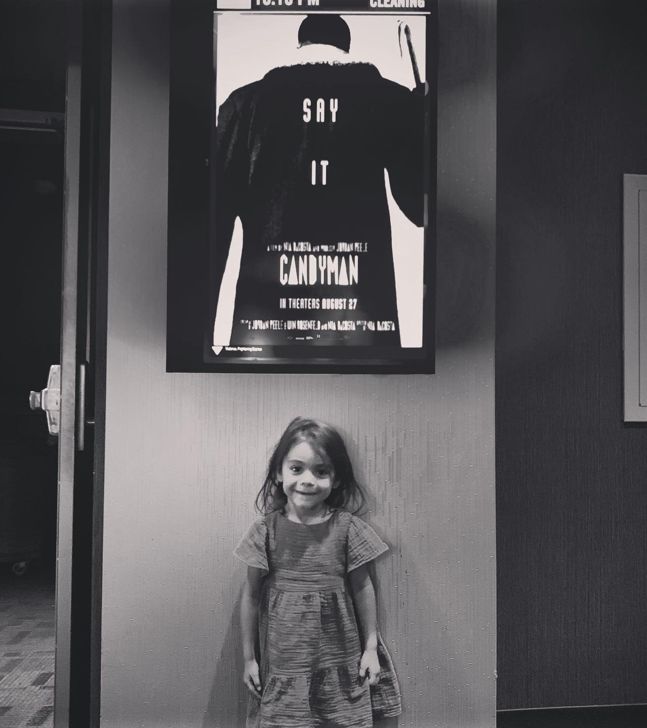 A black and white picture of Noe standing in front of a "Candyman" movie poster.