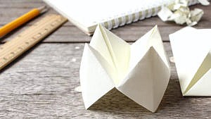A picture of a paper chatterbox on a wooden table with some other stationery.