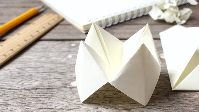 A picture of a paper chatterbox on a wooden table with some other stationery.