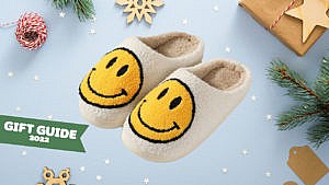 A set of fluffy slippers with smiley faces on them on a holiday themed background.