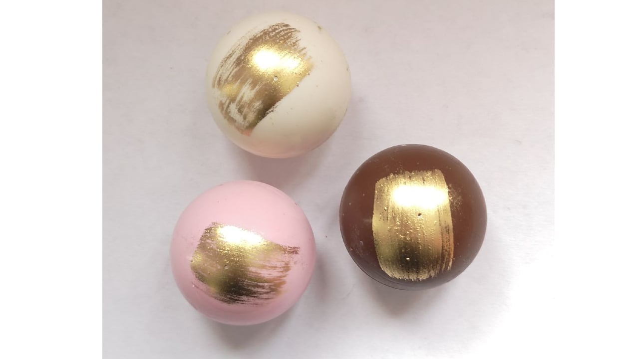 three mini hot chocolate bombs in white, pink and chocolate with gold flecks